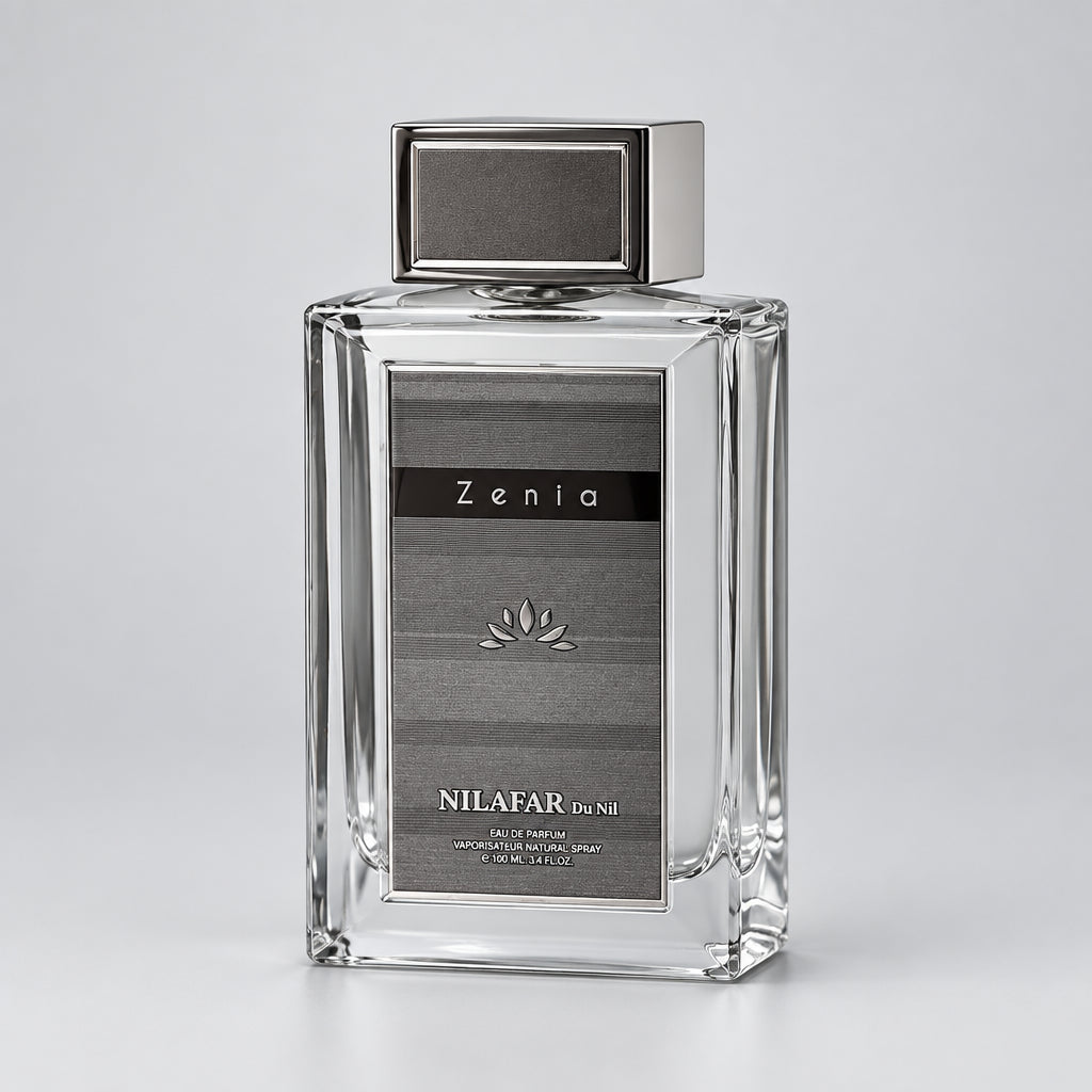A rectangular clear glass perfume bottle with a metallic bronze cap and a dark gray label reading 'Zenia' and 'NILAFAR Eau de Nil'.